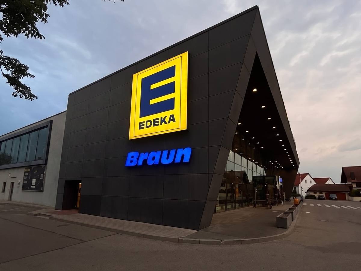 Das EDEKA Braun Center in der Dämmerung: der dunkle, spitz zulaufende Baukörper mit beleuchtetem EDEKA-Schild und blauem Braun-Schriftzug über dem Eingang.